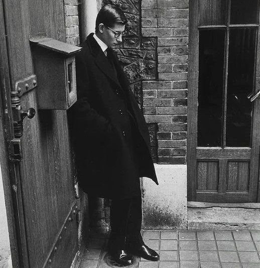 A young Yves Saint Laurent standing alone after attending the funeral of his mentor, Christian Dior